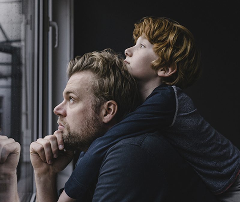 child piggy back on father and both are looking out window